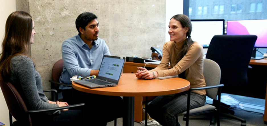 Two graduate students and a supervisor sitting at a round table having a discussion.