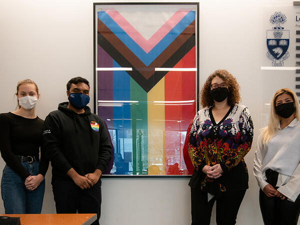 Portrait of members of the PharmaPride student group with Dean Lisa Dolovich posing in front of inclusion pride flag at the Leslie Dan Faculty of Pharmacy