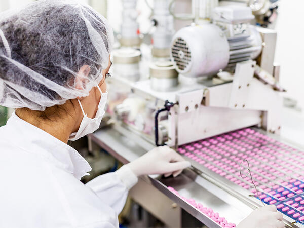 Person working with selection of pink pills on a production line