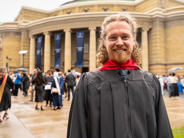 PharmD for Pharmacists Graduate Brandon Toner photographed in graduation regalia with University of Toronto's Convocation Hall in the background