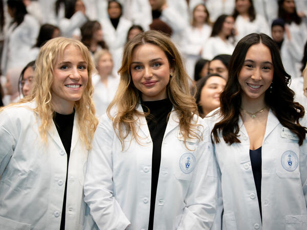 Three female-presenting students wearing white lab coats with circular Pharmacy crest