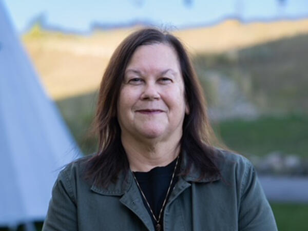 Deborah_Emery_Feature Portrait of woman standing outdoors with grassy hill and blue sky in background